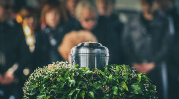 A group of people are standing around a urn at a funeral.