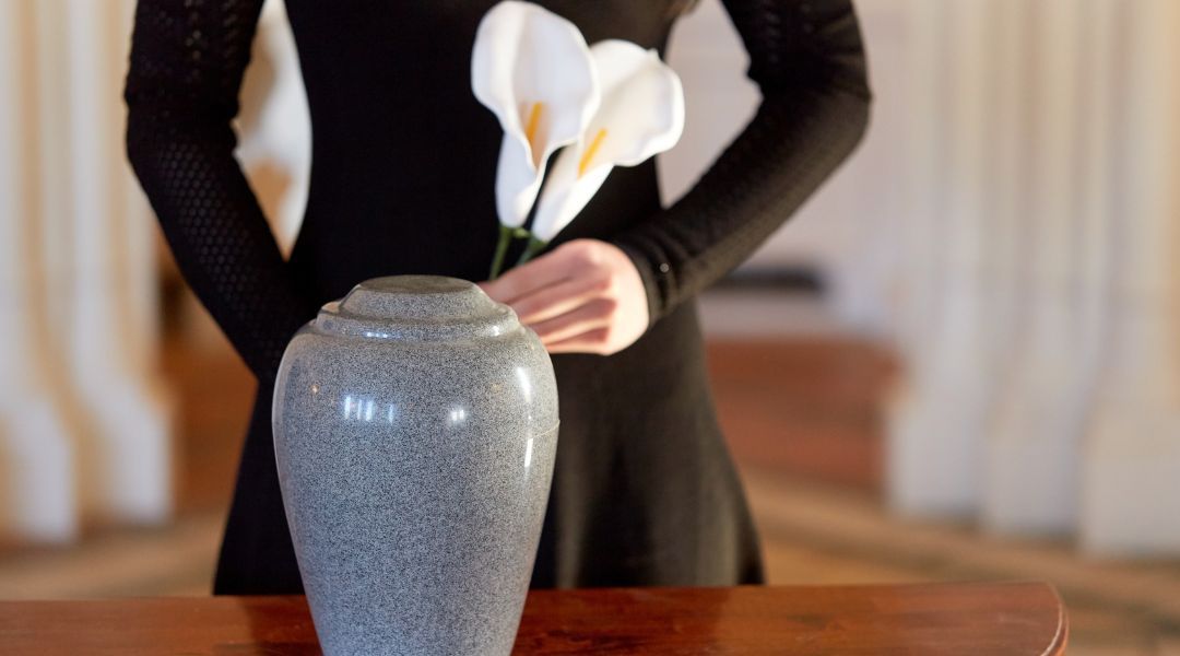 A woman in a black dress is holding a vase with white flowers in it.