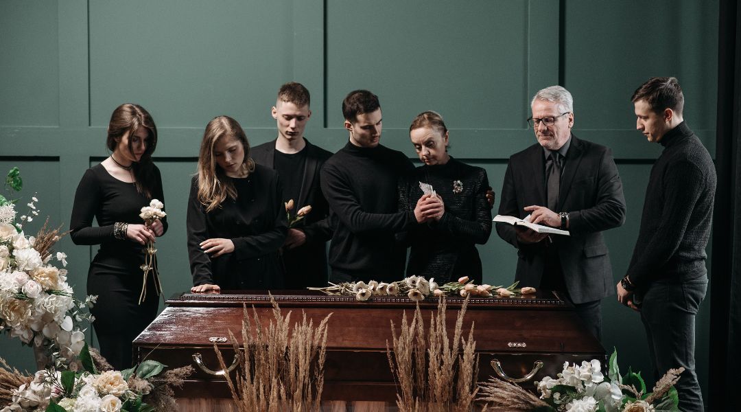 A group of people are standing around a coffin at a funeral.