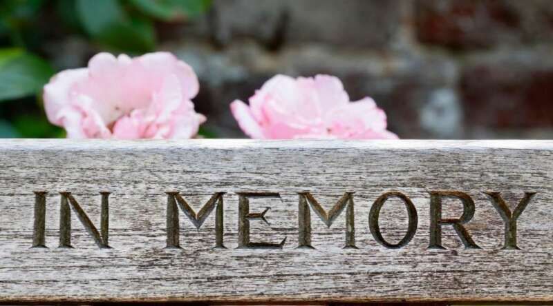 A wooden sign that says `` in memory '' with pink flowers in the background.
