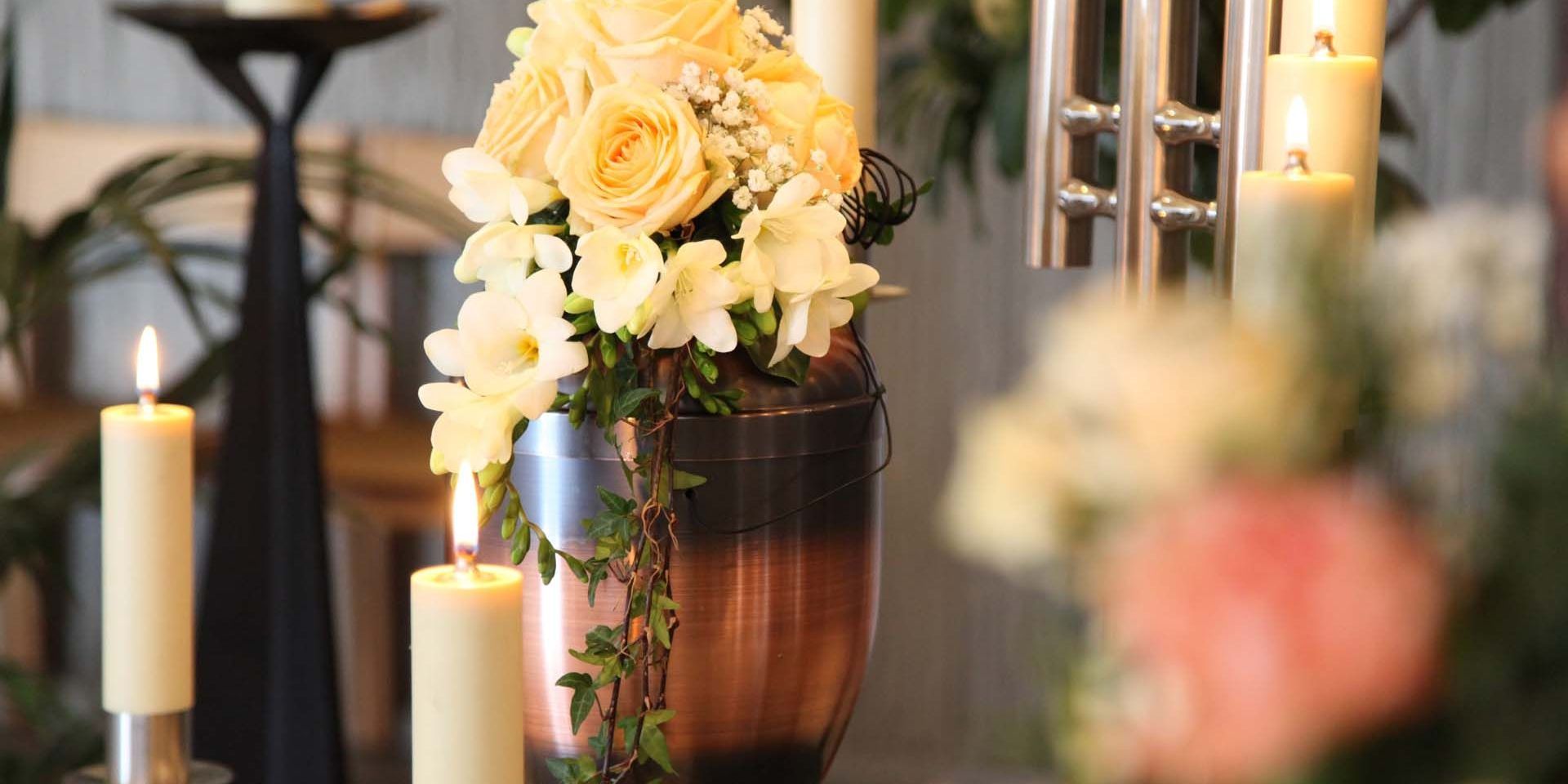 a black urn with leaves on it sits on a table next to a red rose