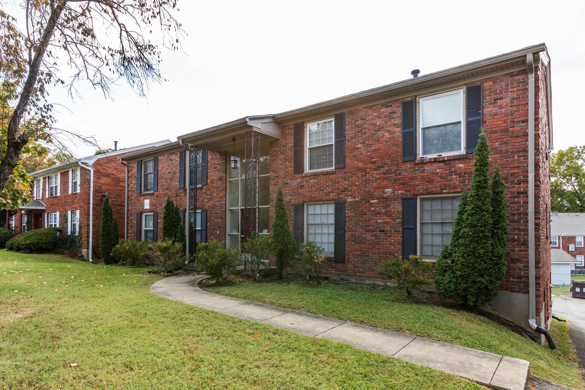 A brick apartment building with black shutters and a sidewalk in front of it.