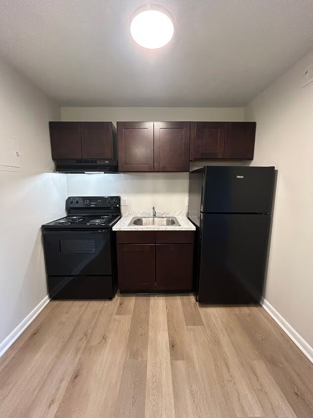 A kitchen with a stove , refrigerator , sink and cabinets.
