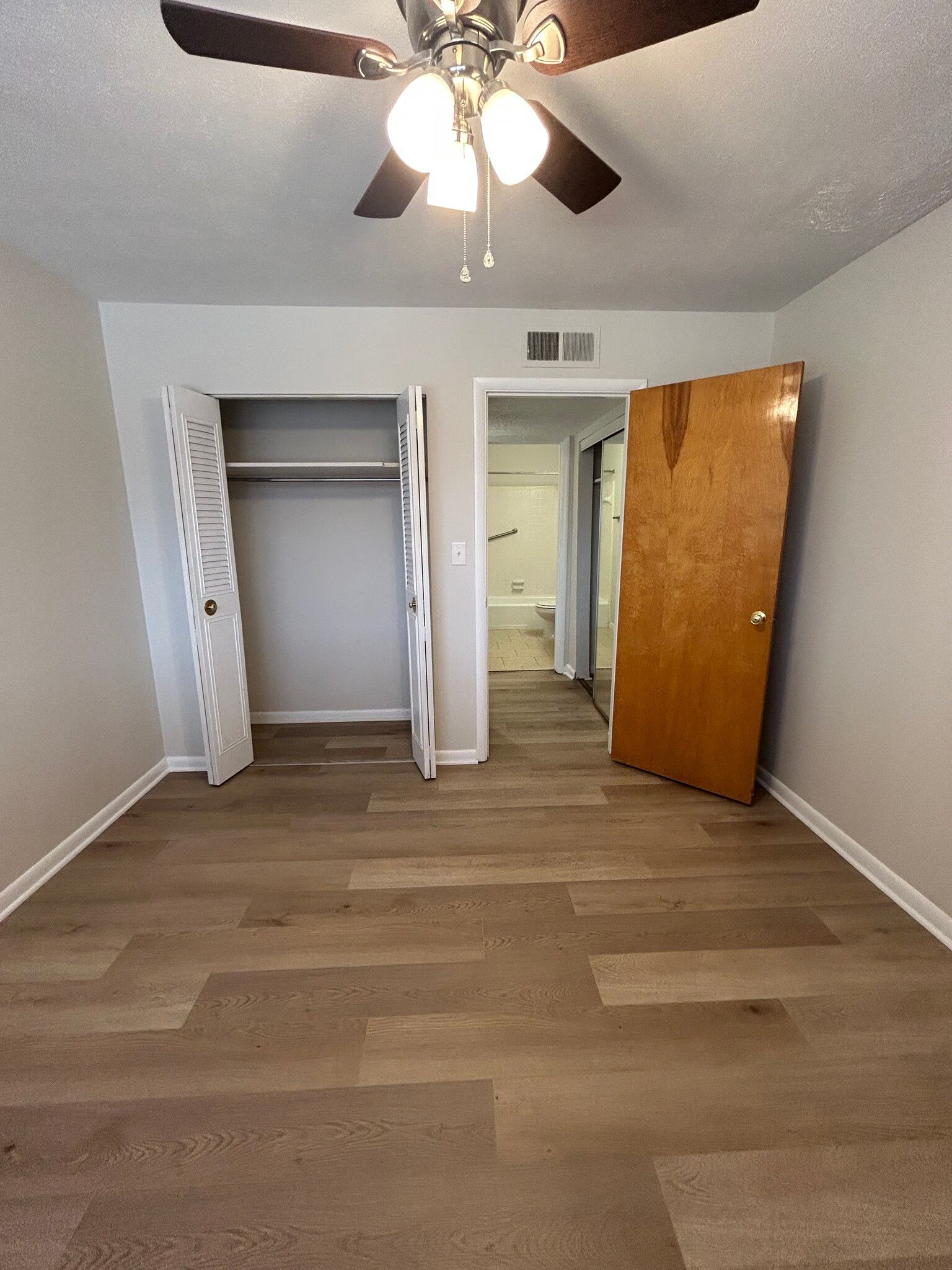 An empty bedroom with hardwood floors and a ceiling fan.