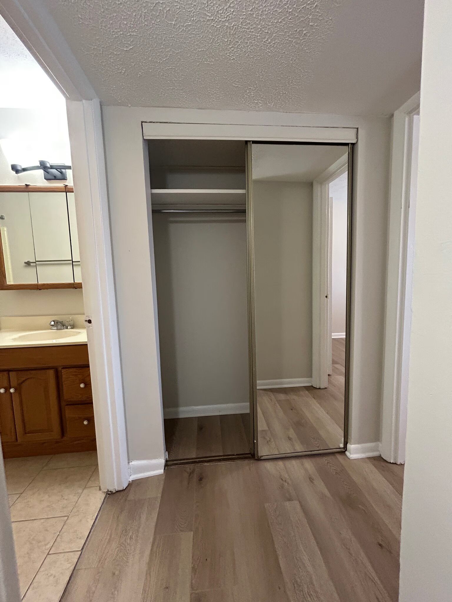 There is a closet with a mirror in it and a bathroom in the background.