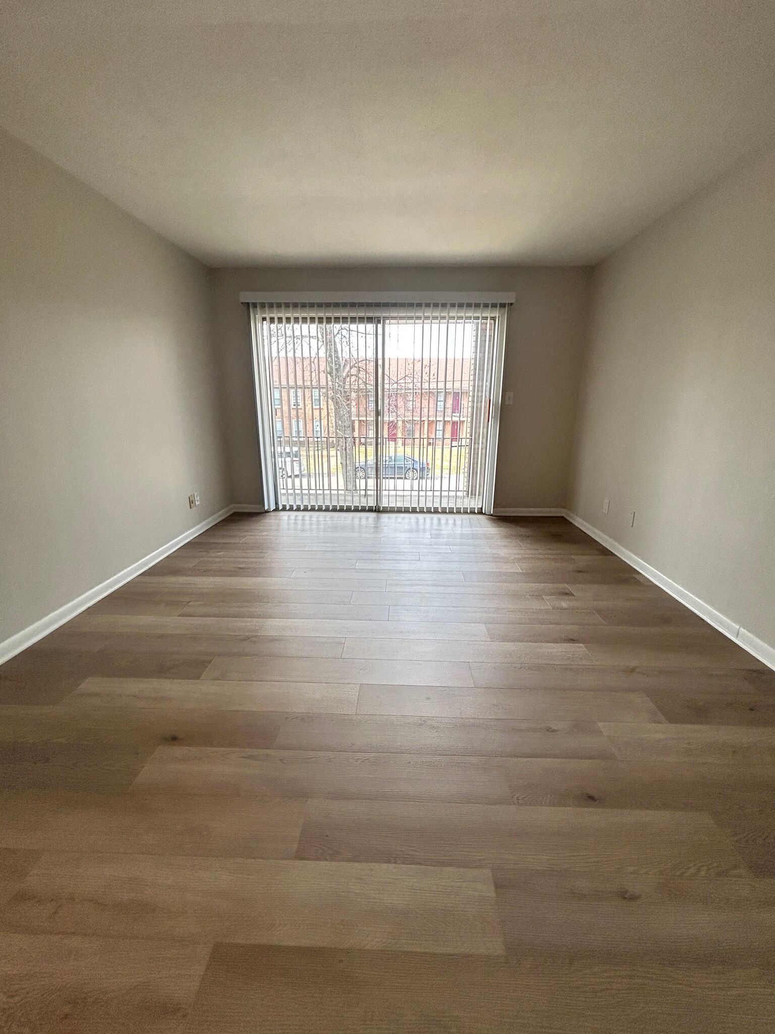 An empty living room with hardwood floors and sliding glass doors.