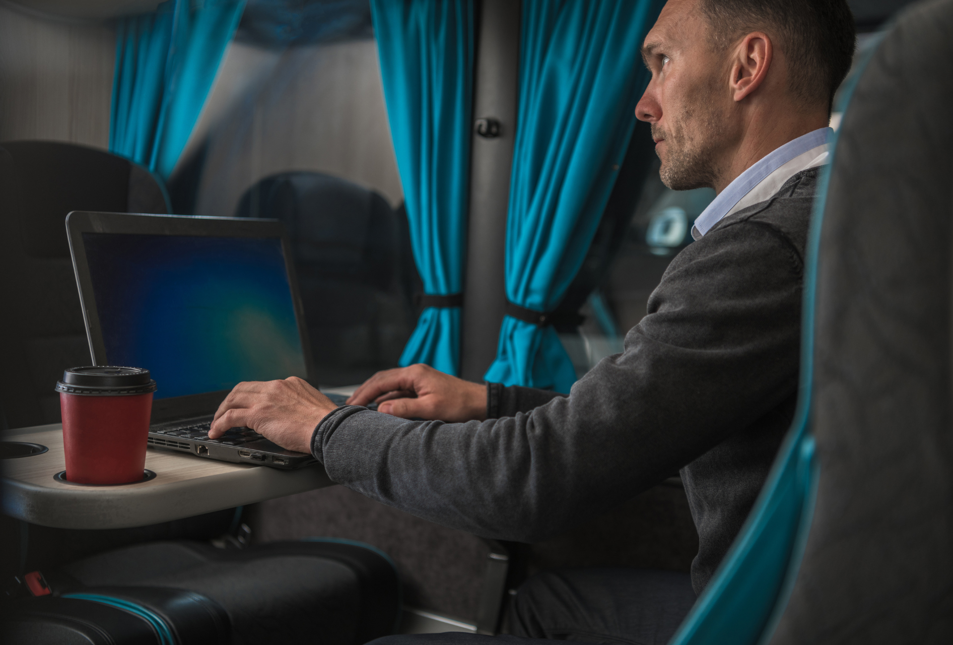 A man is sitting in a bus using a laptop computer.