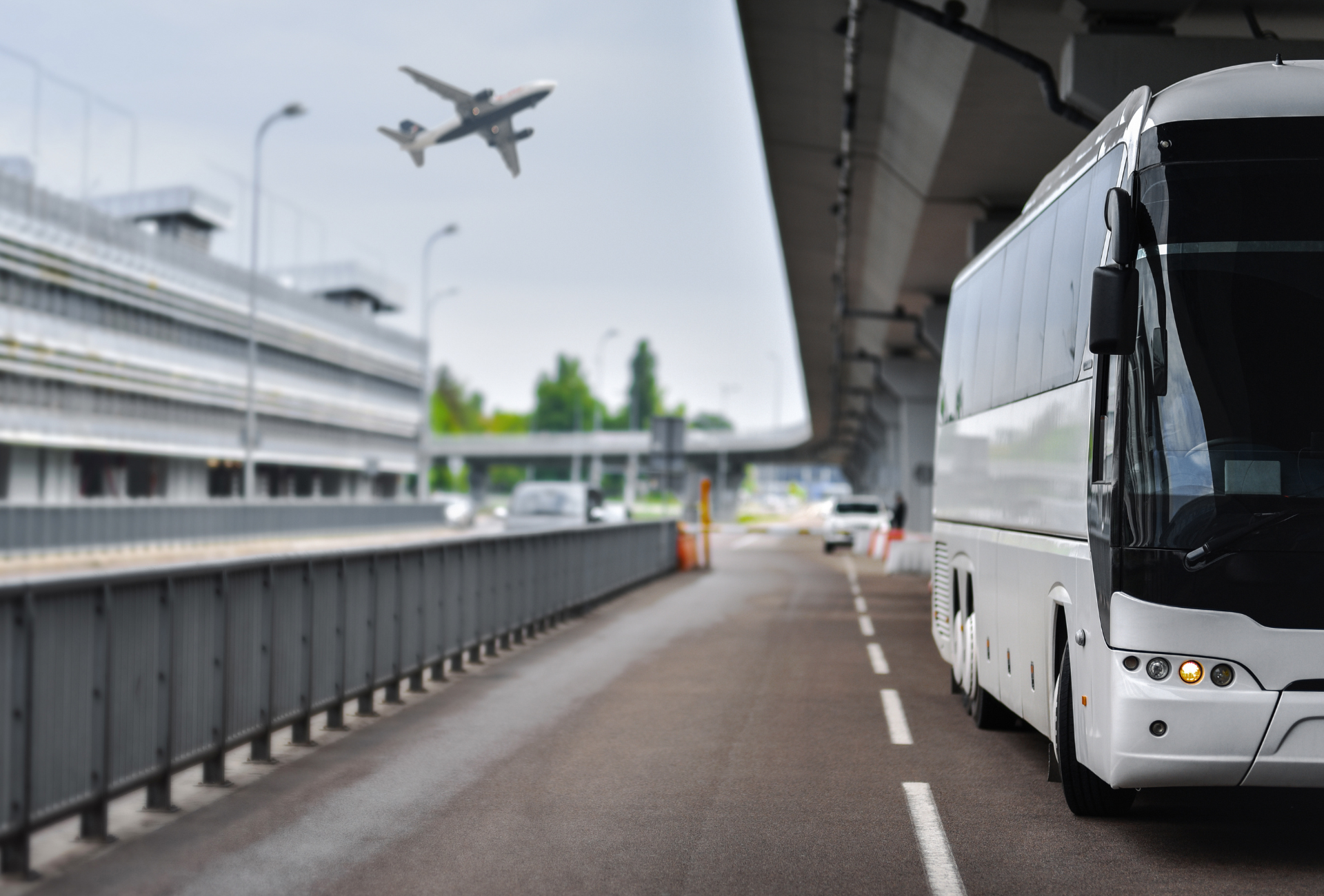 A bus is driving down a highway with a plane flying in the background.