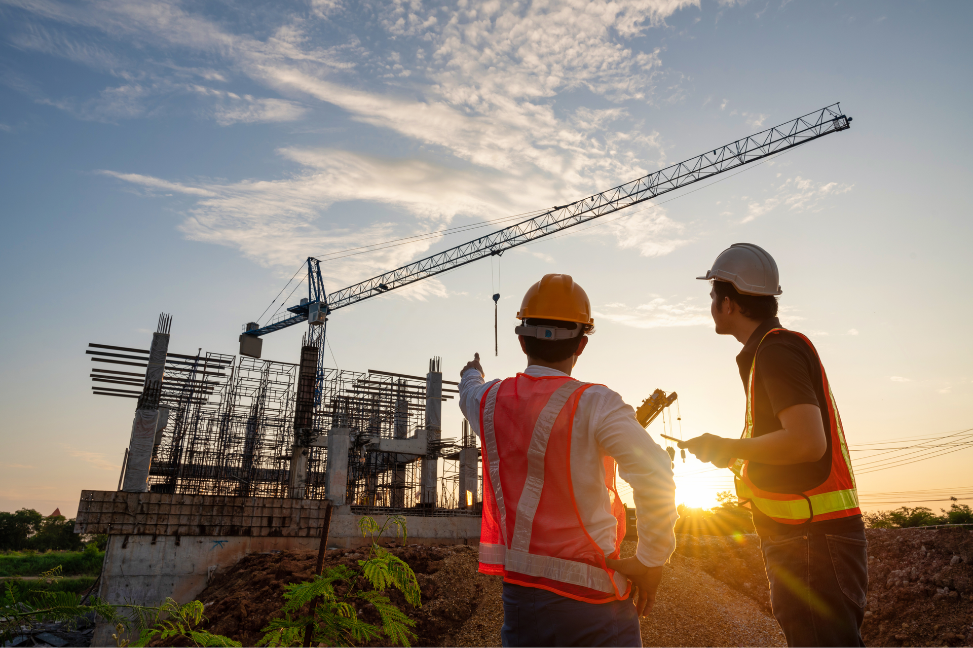 Construction workers at sunset, pointing towards a building under construction, crane in background.