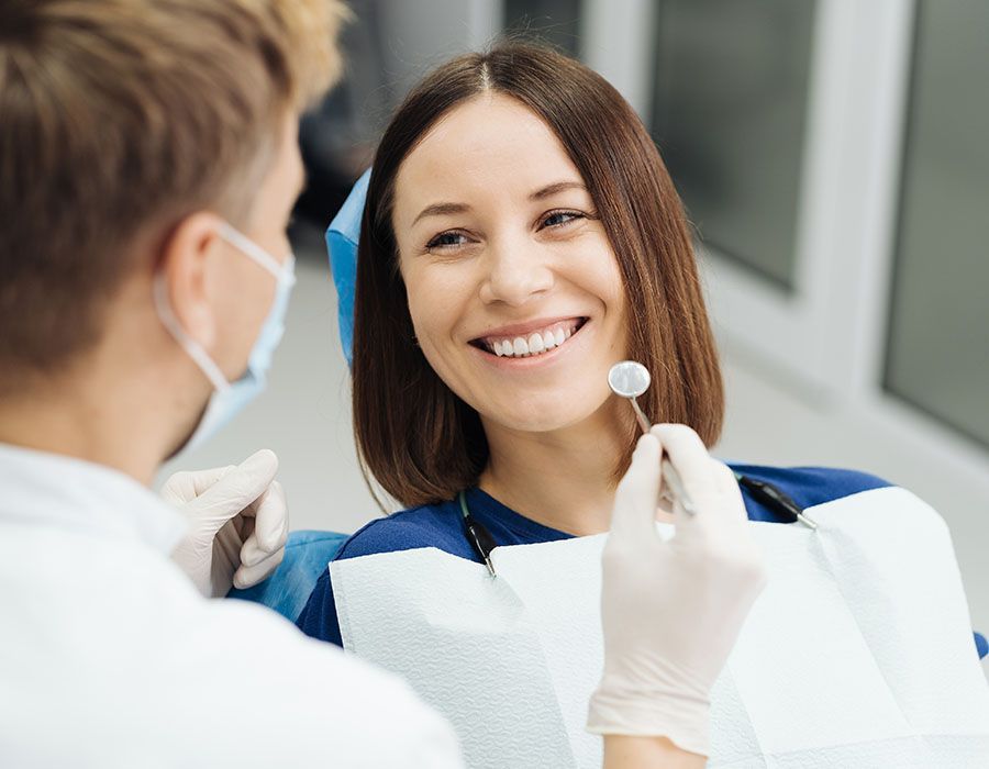 Dentist examining a smiling patient in a clinic, with a white mask and dental bib visible