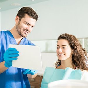 Dental staff showing a tablet to a smiling patient in a clinic room