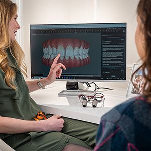 Two people review 3D teeth models on a computer in a dental consultation office.