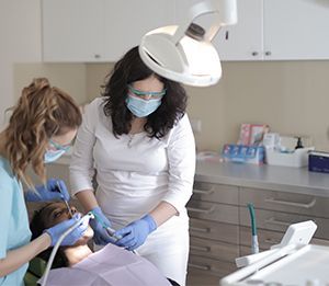 Dentist and assistant wearing masks treating a patient under a dental lamp