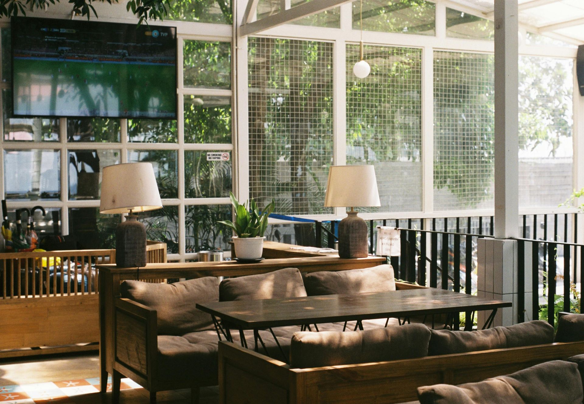 Cozy indoor dining area with couches, lamps, TV, and large windows looking out to greenery.