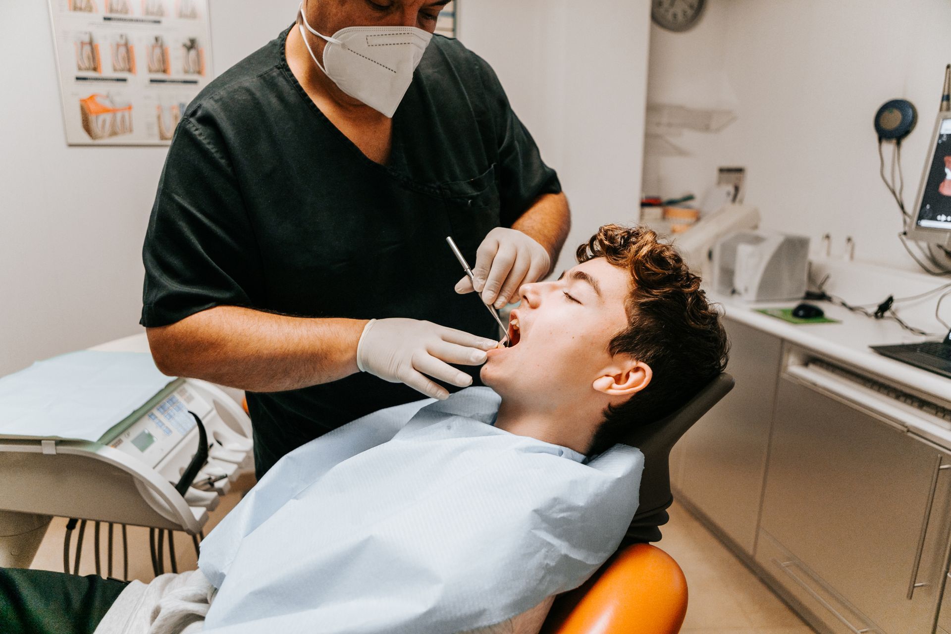 A dentist is examining a young man 's teeth in a dental chair.