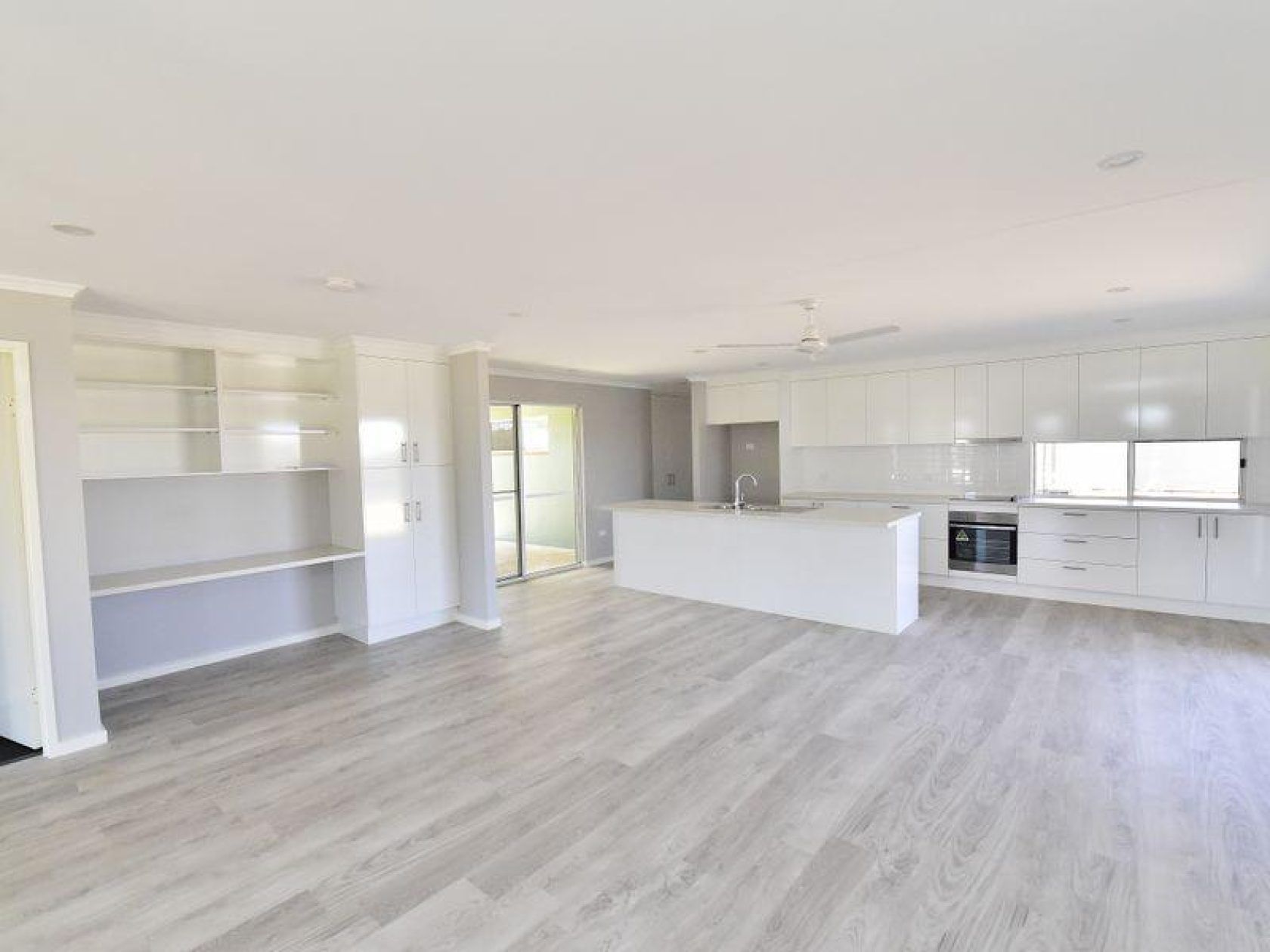 Modern open-plan living space with white kitchen, gray flooring, and sliding glass doors.