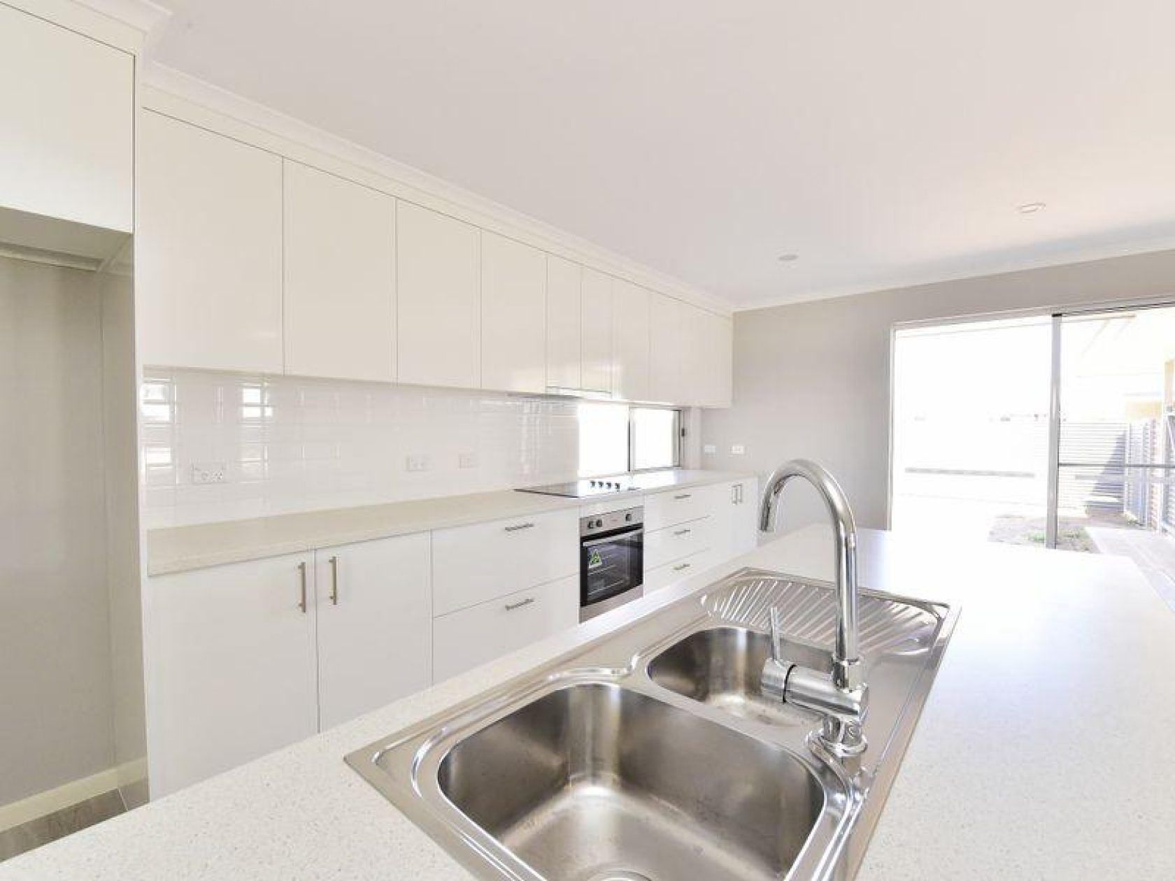 Modern kitchen with white cabinets, stainless steel sink, and sliding glass door.