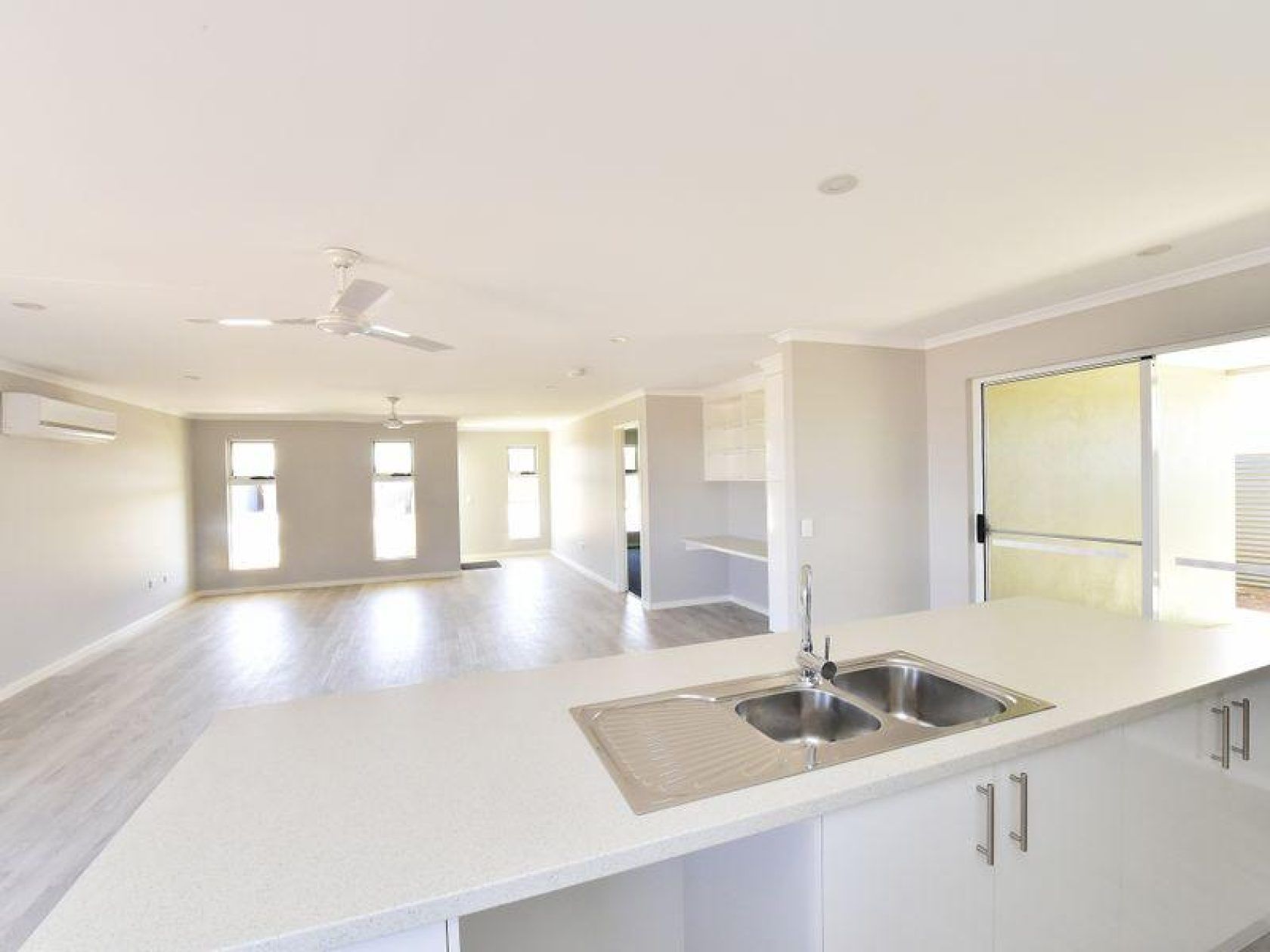Modern kitchen with white countertop, sink, and open layout to living area with large windows.