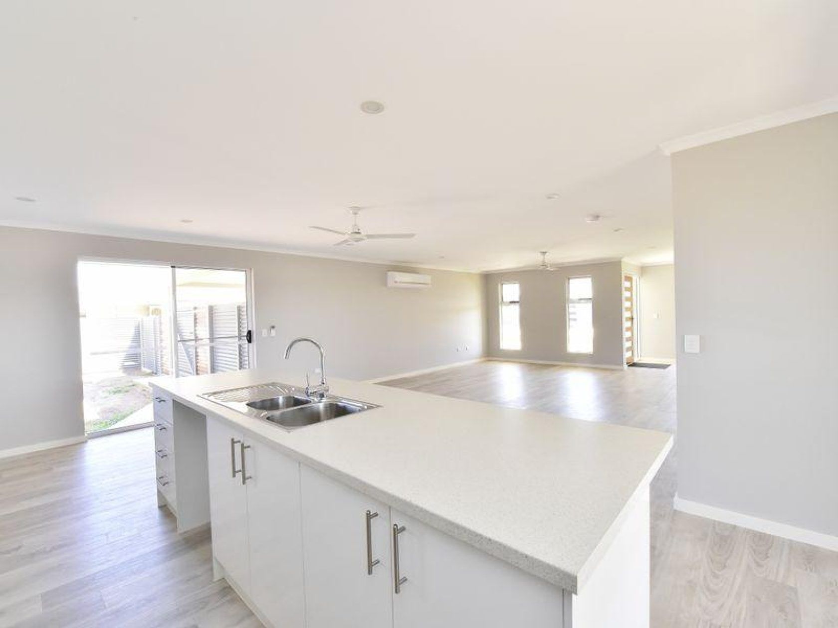 Open-concept kitchen with island, sink, white countertops, and light gray walls, leading into living space.
