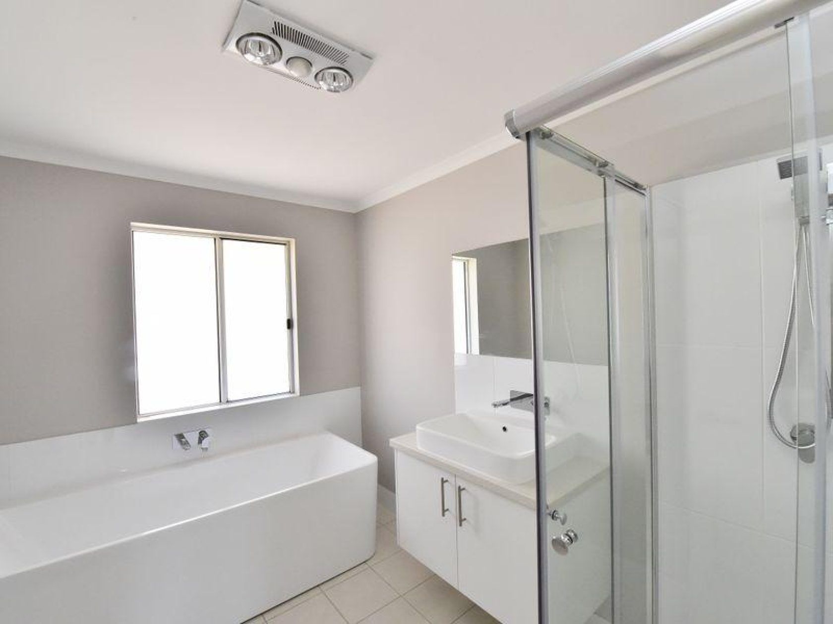 Modern white bathroom with tub, shower, vanity, window, and exhaust fan; gray walls.