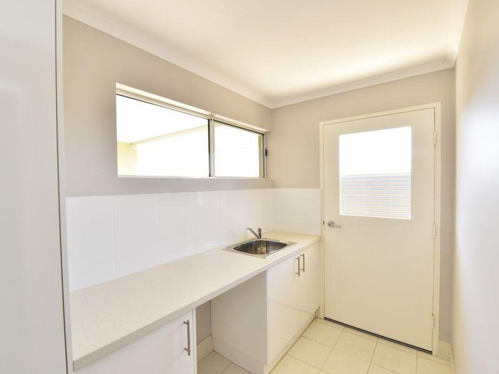 Laundry room with white cabinets, countertop, sink, window, and door.