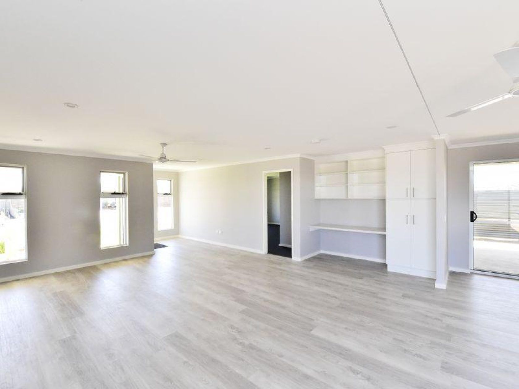 Spacious, bright interior with light wood floors, gray walls, white built-ins, and large windows.