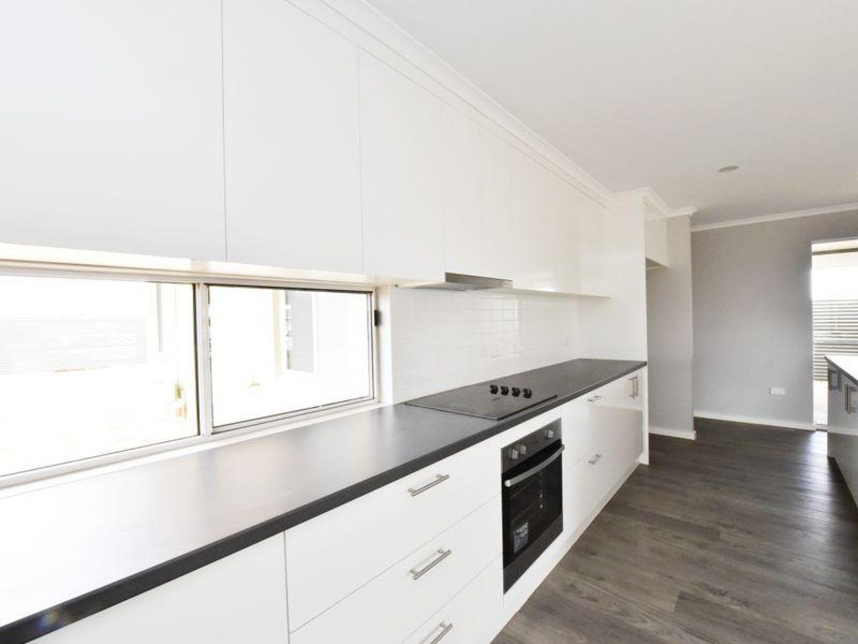 Modern white kitchen with black countertops, built-in oven, and a window.