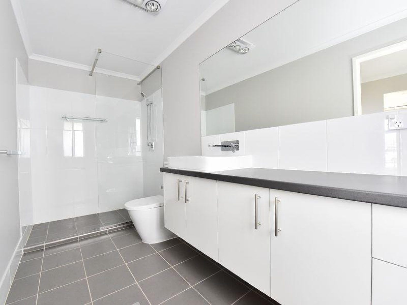 Modern, white bathroom with grey tiled floor and cabinetry, rectangular mirror, and shower.