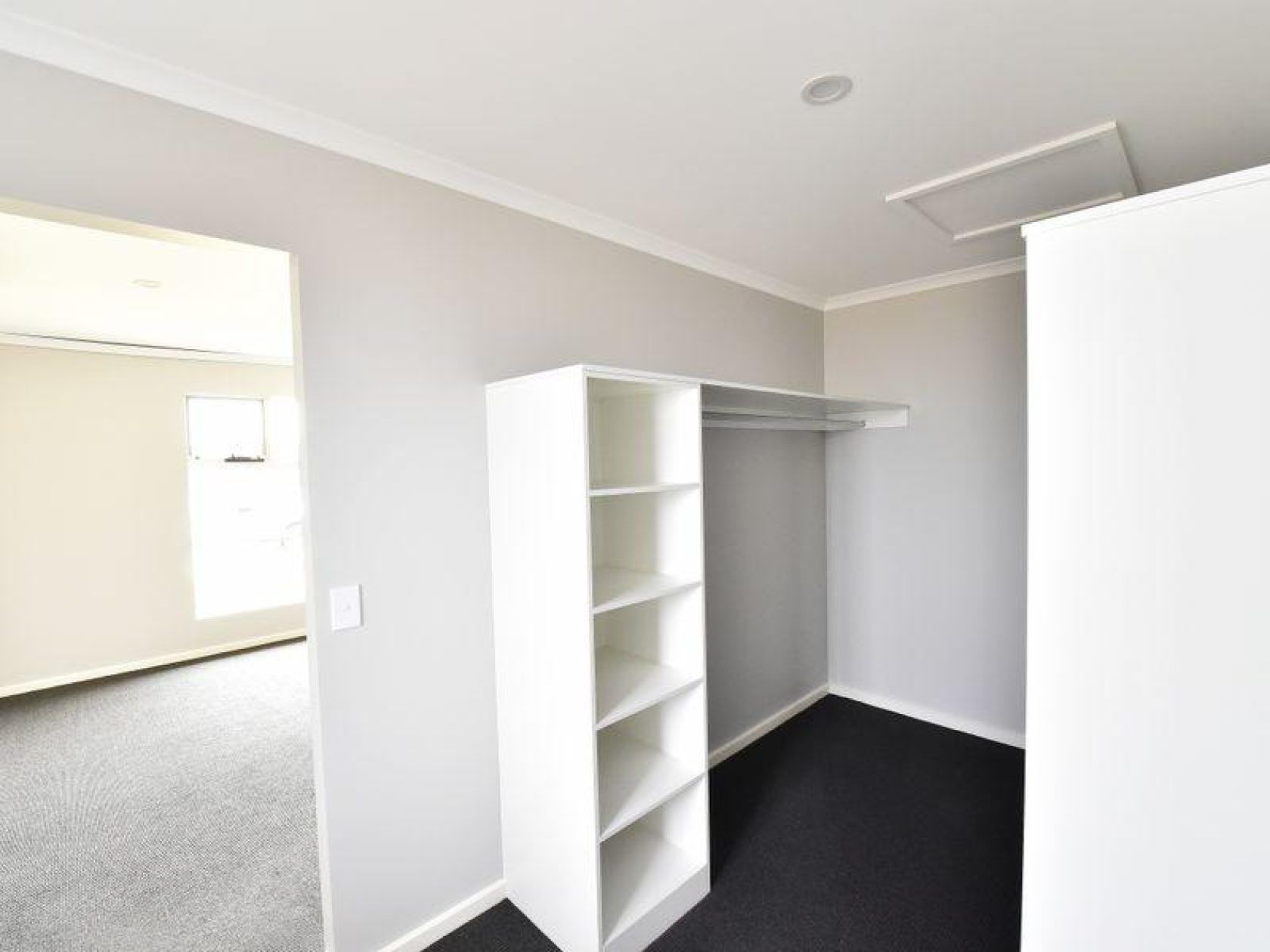 Empty room with white shelves, closet rod, and door to another room; gray walls, dark carpet.