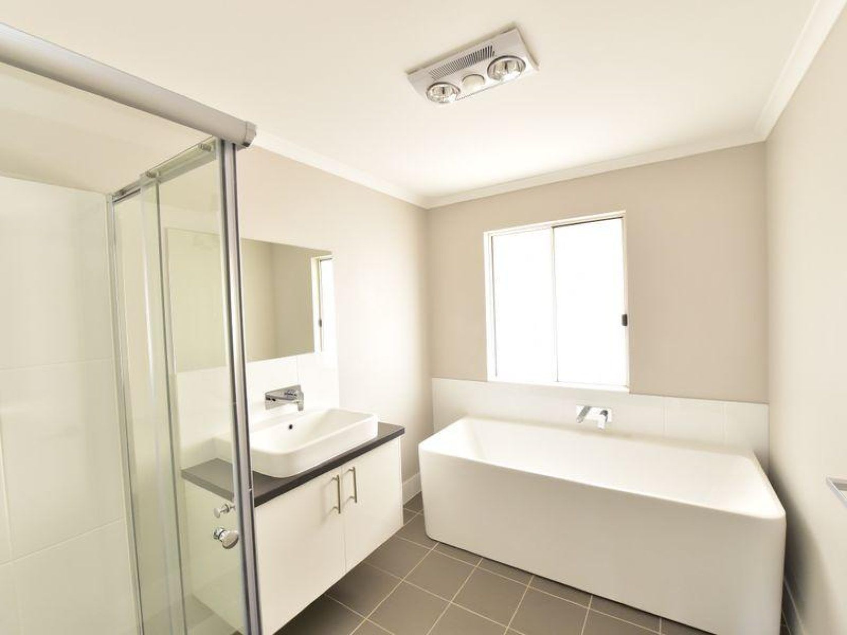 Modern bathroom with a white tub, shower, vanity, and window; neutral-colored walls and floor.