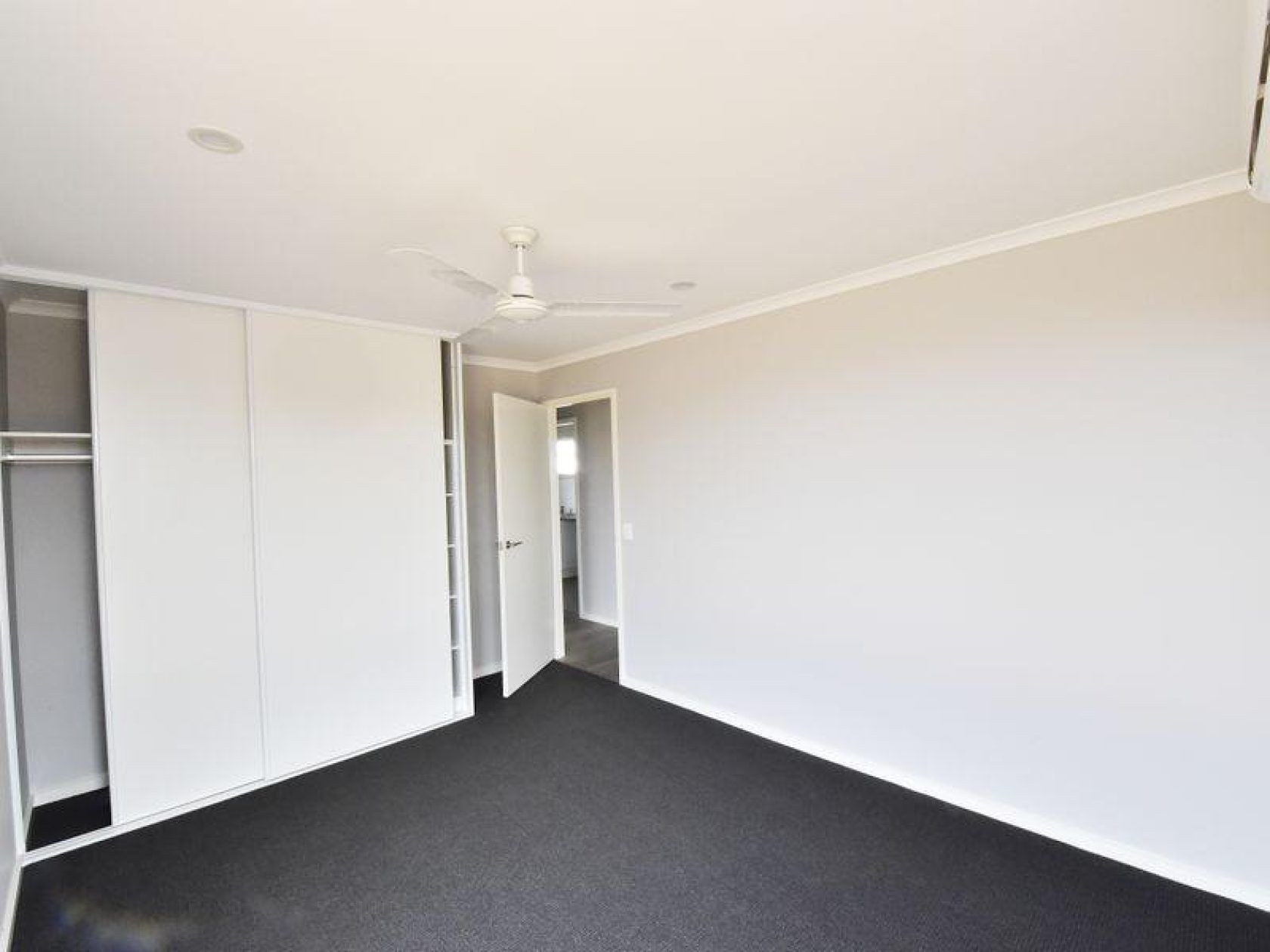 Empty bedroom with white walls, dark carpet, and closet.