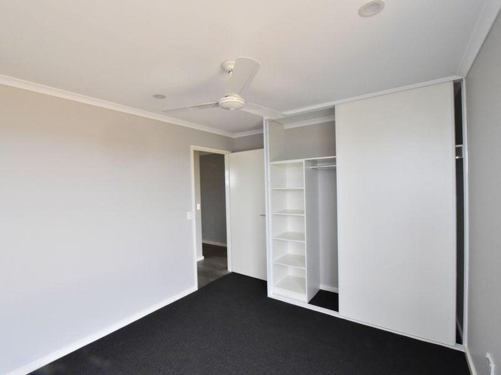 Empty bedroom with black carpet, white closet, and gray walls.