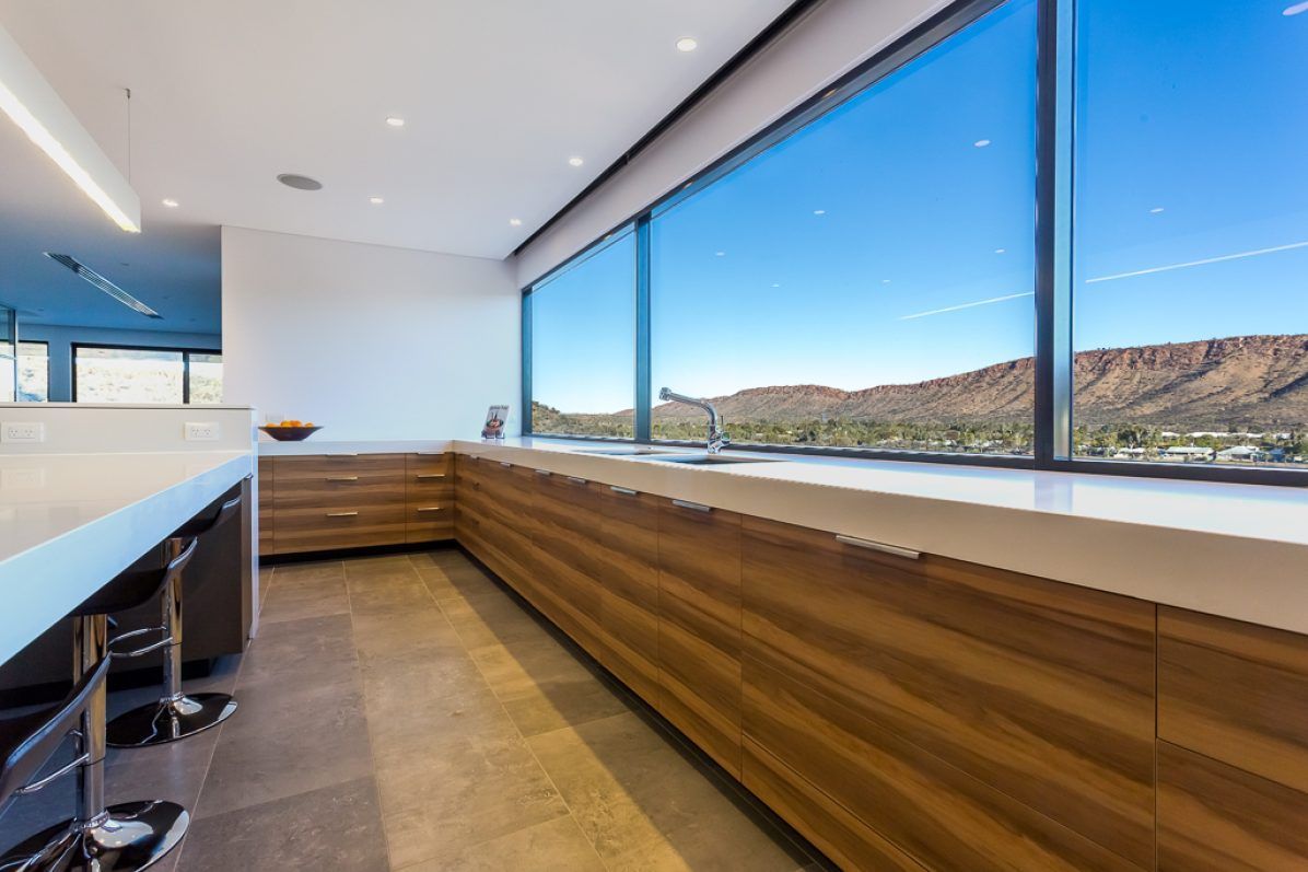 Modern kitchen with wood cabinets, large windows overlooking a mountain range, and bar seating.
