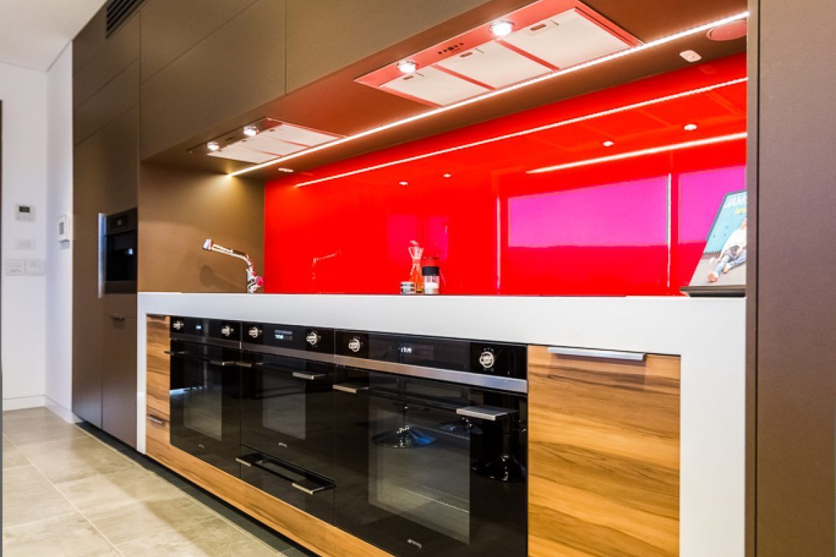 Modern kitchen with red backsplash, wooden cabinets, and built-in black ovens.