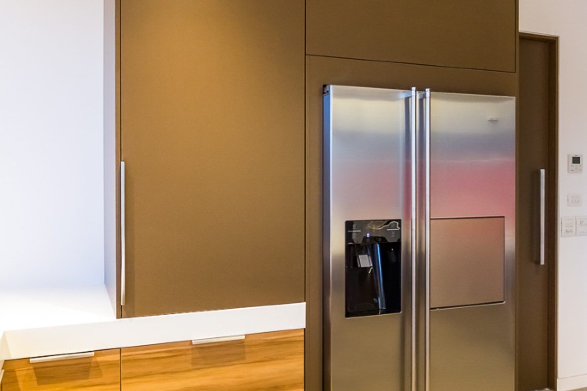 Stainless steel refrigerator in a modern kitchen with brown cabinets and a white countertop.