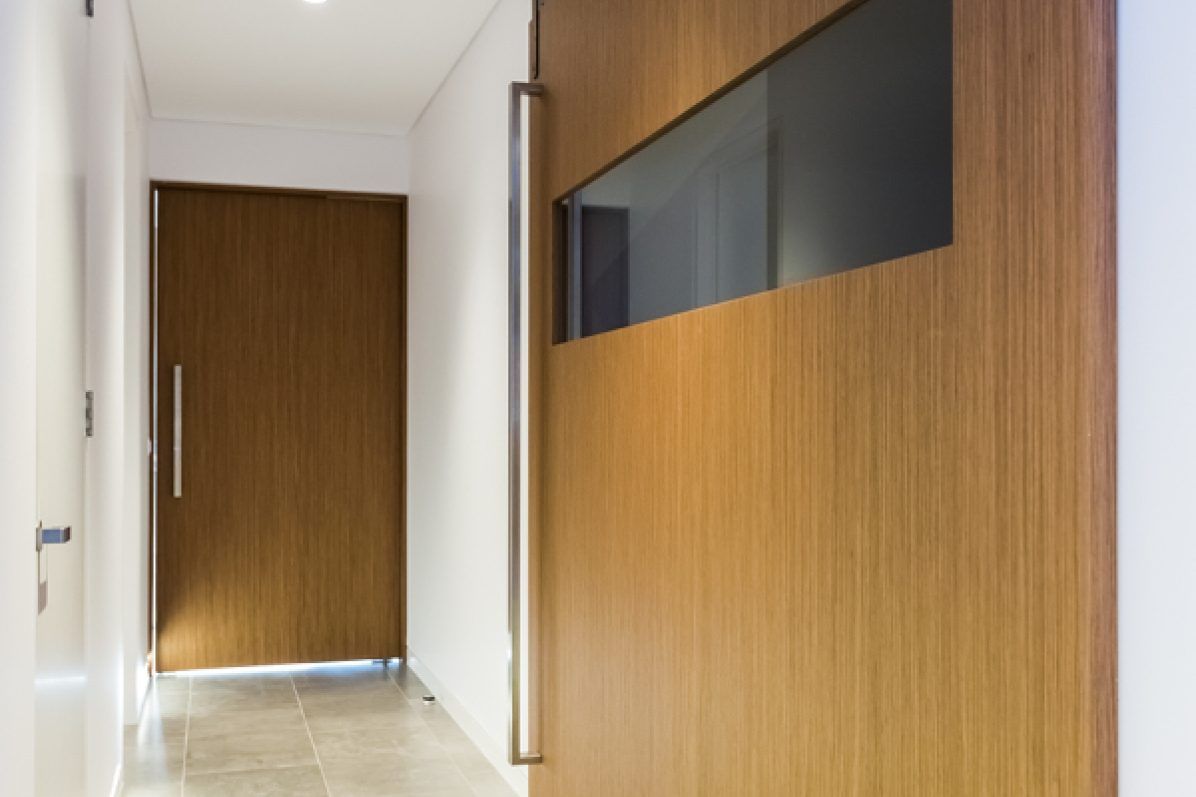 Narrow hallway with a wooden door, glass window, and a brushed-metal handle.