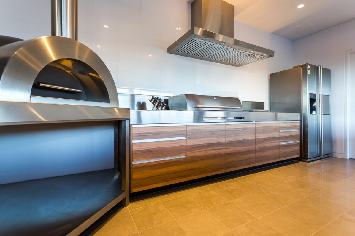 Modern kitchen with stainless steel oven, countertops, and refrigerator; wood cabinets.