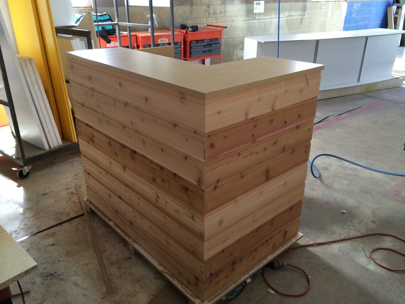 Wooden bar with light-colored countertop and a base of horizontal cedar planks. Indoors, workshop setting.