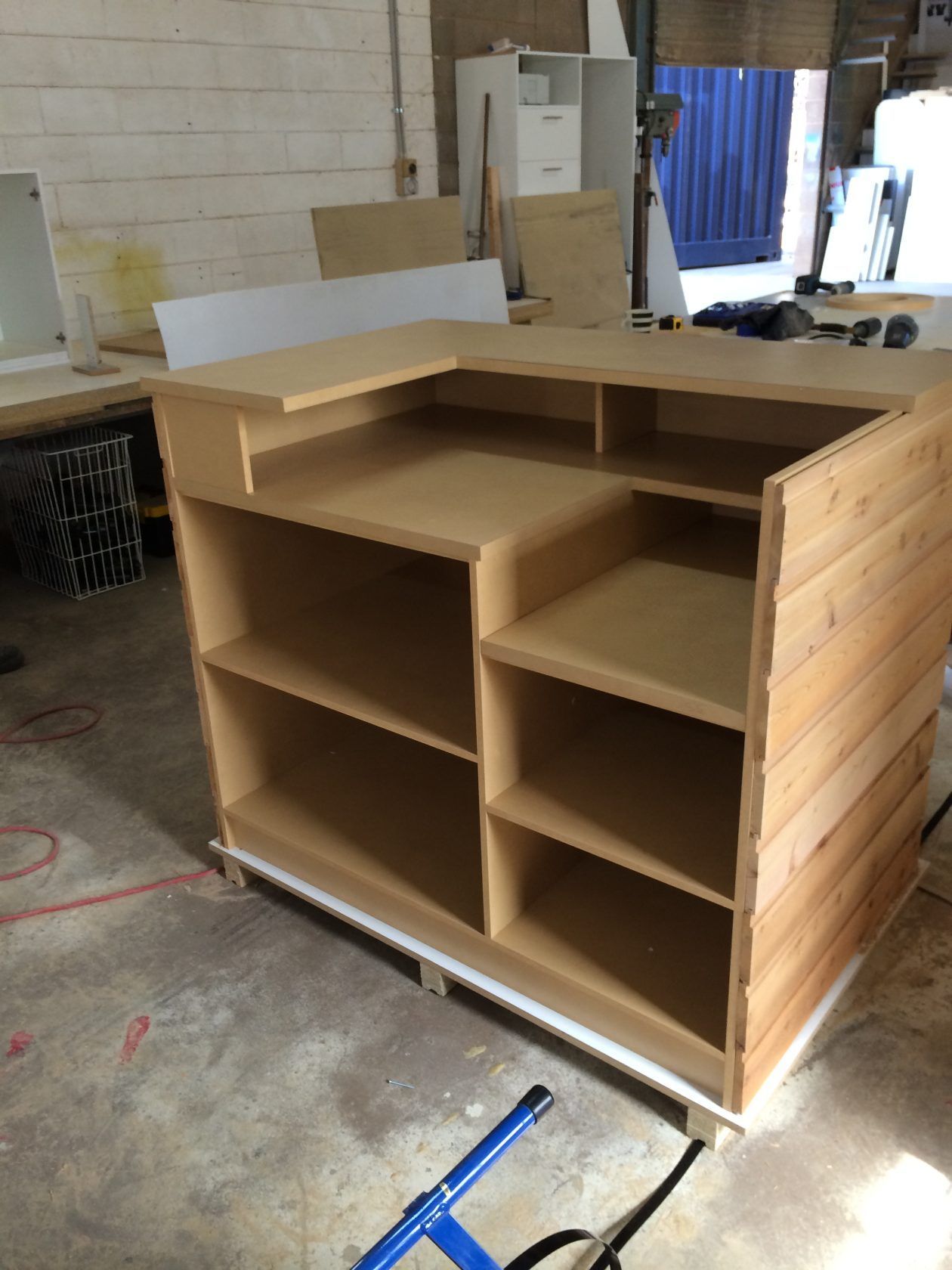 Wooden L-shaped counter under construction with shelves and a light wood facade.
