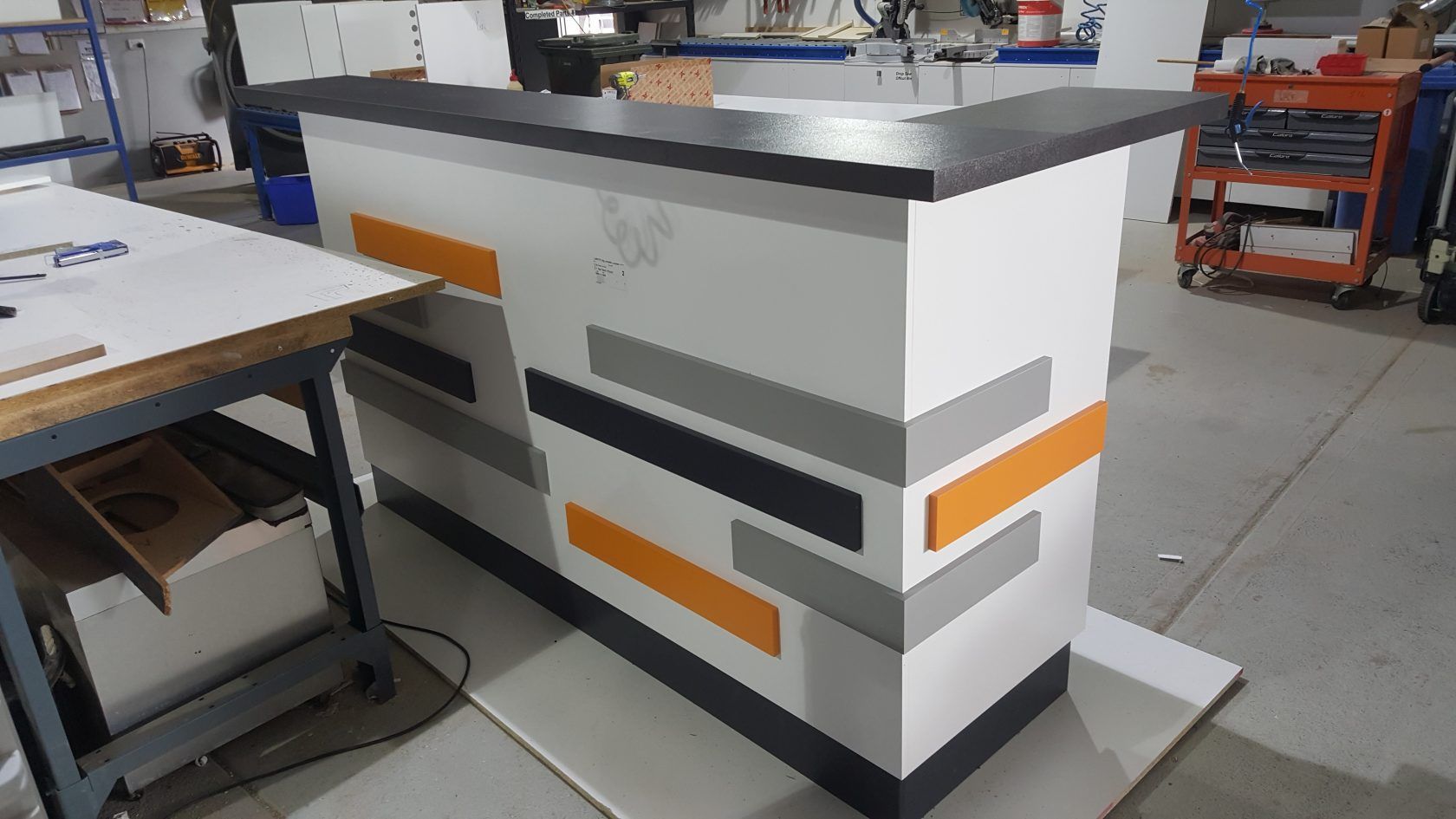 Modern bar with white, orange, gray, and black accents in a workshop setting.