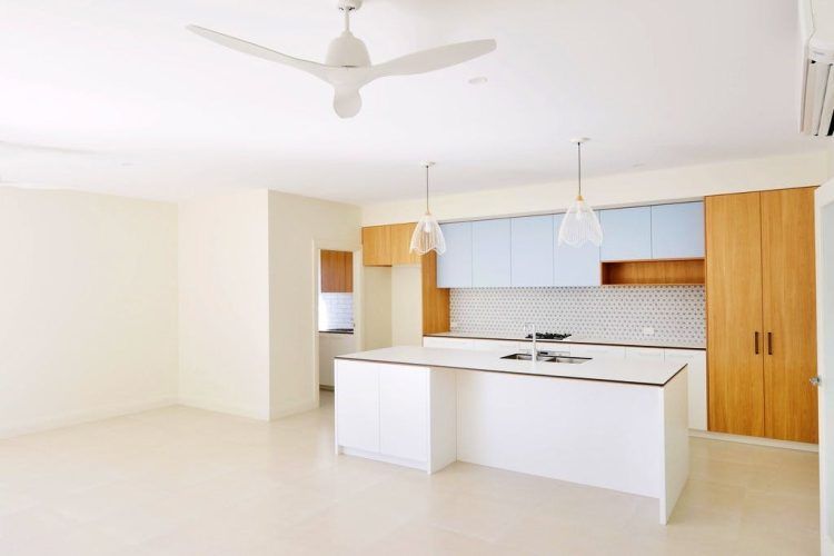 Empty modern kitchen with white island, wood cabinets, and blue upper cabinets.