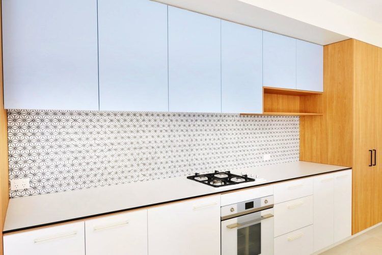 Modern kitchen with light blue cabinets, white countertops, gas stove, and geometric tile backsplash.