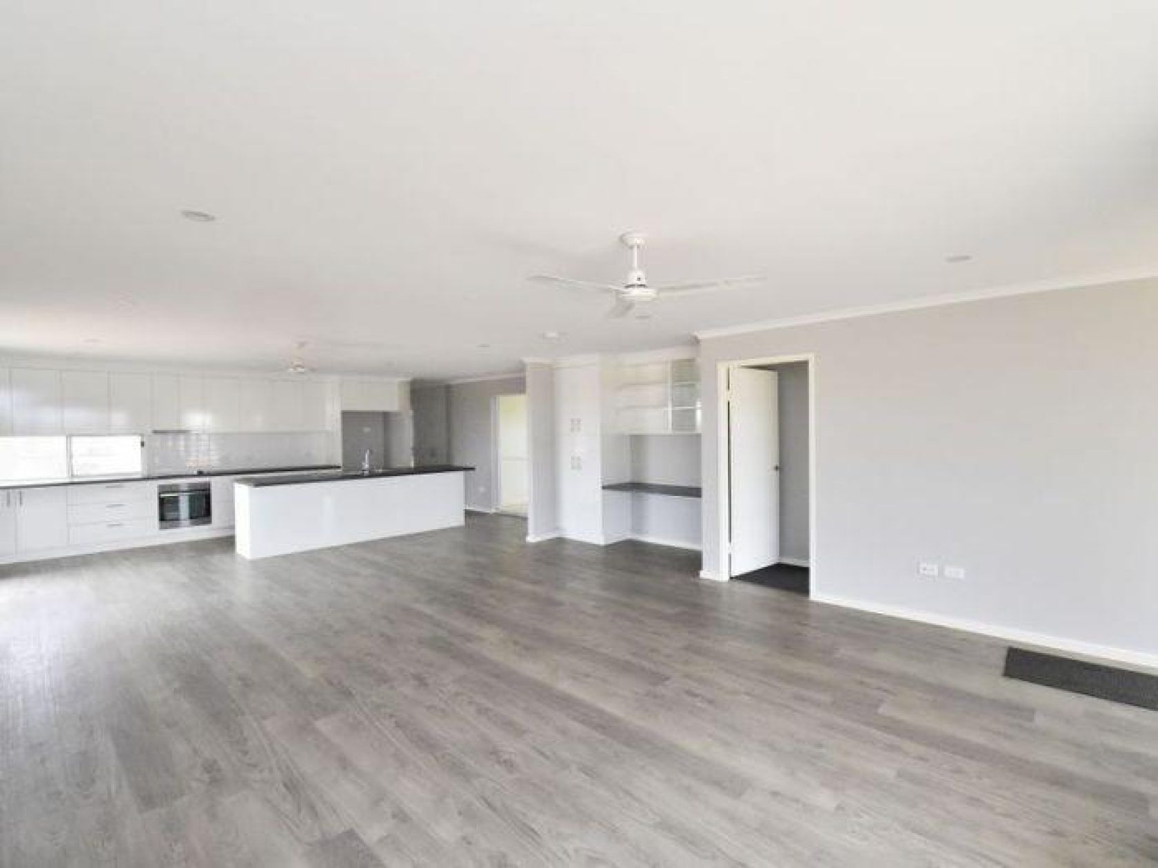 Spacious, open-plan living area with gray floors, white kitchen, and neutral walls.