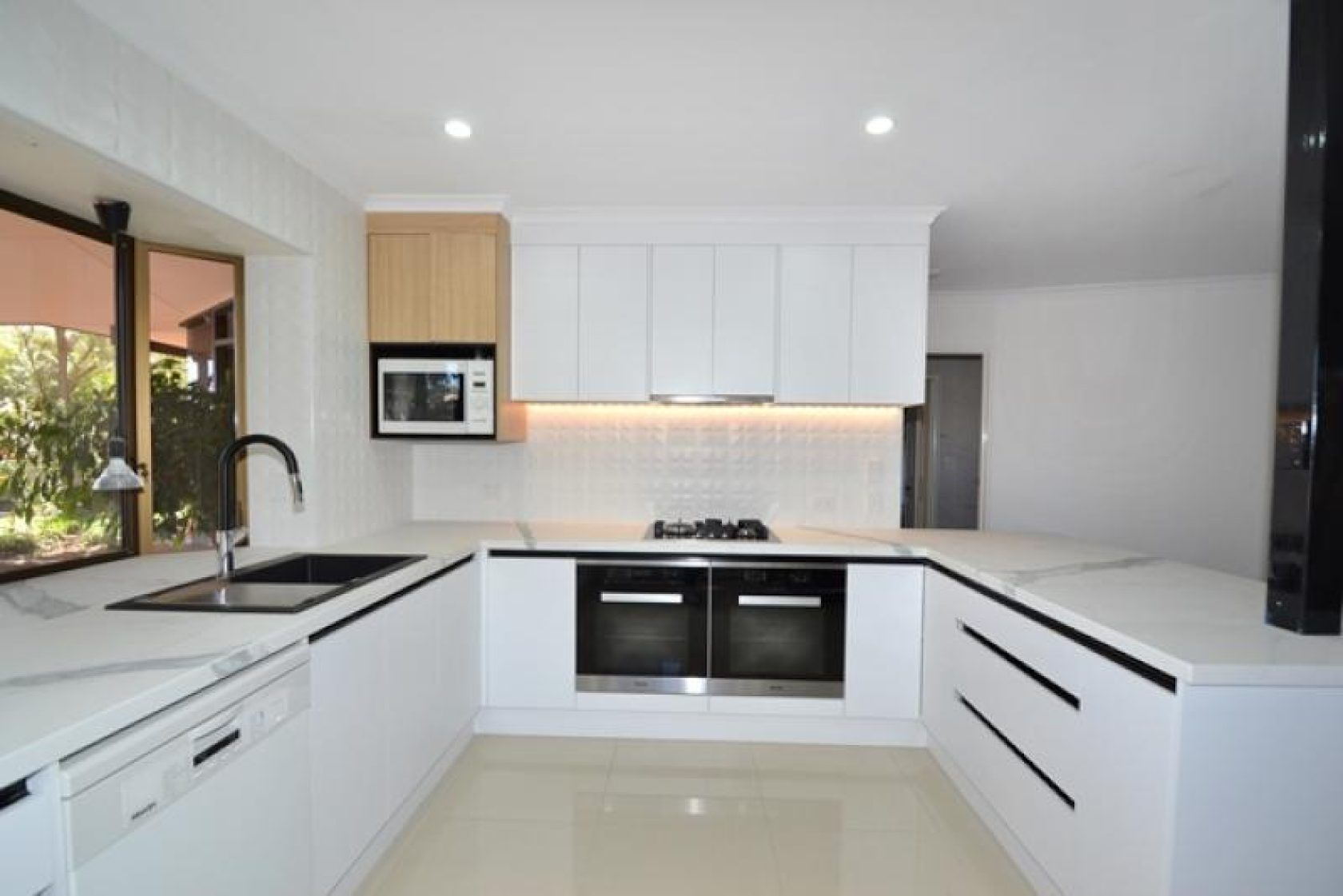 Modern white kitchen with light wood cabinets, black accents, and natural light.