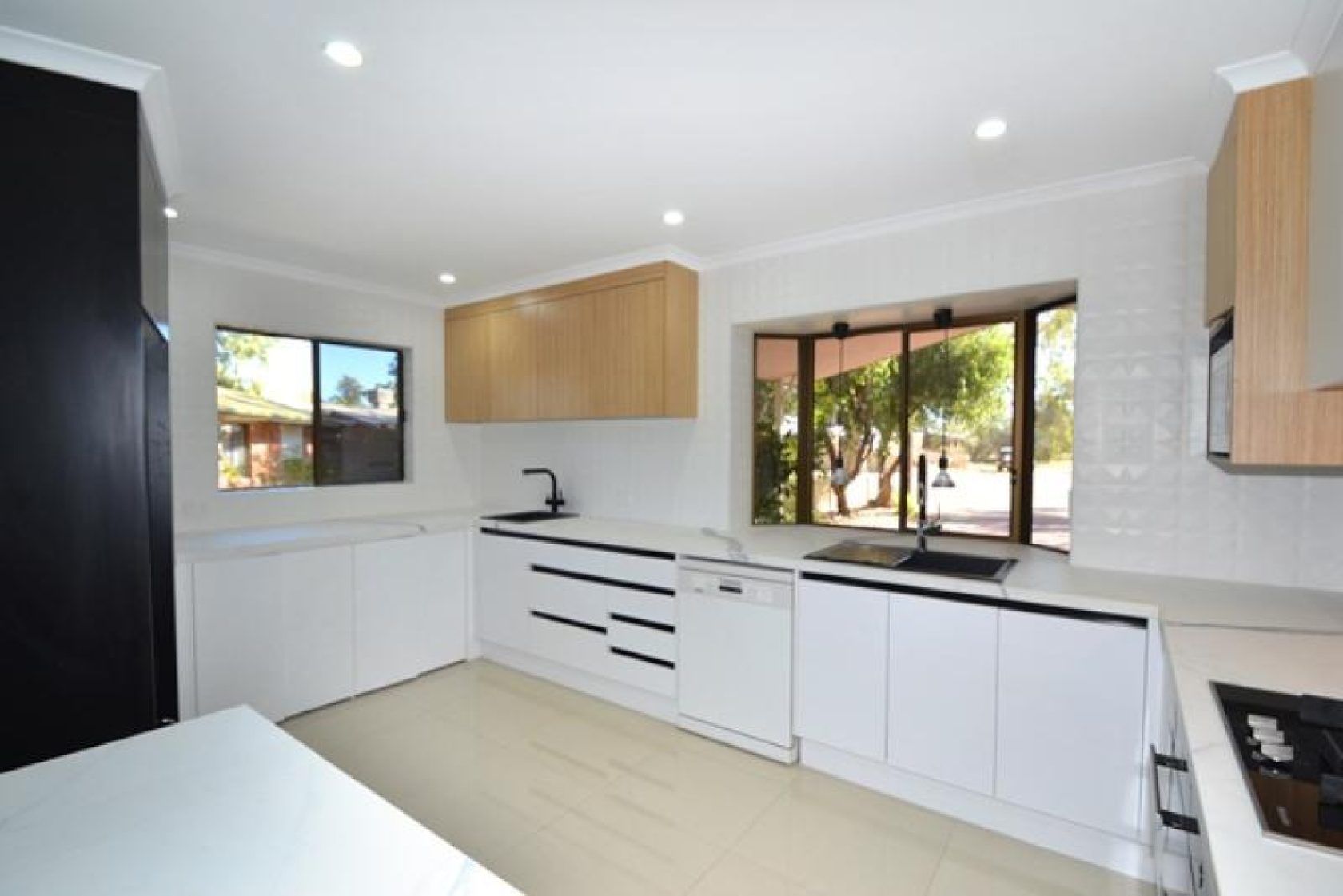 Modern white kitchen with wood accents and a large window overlooking a yard.