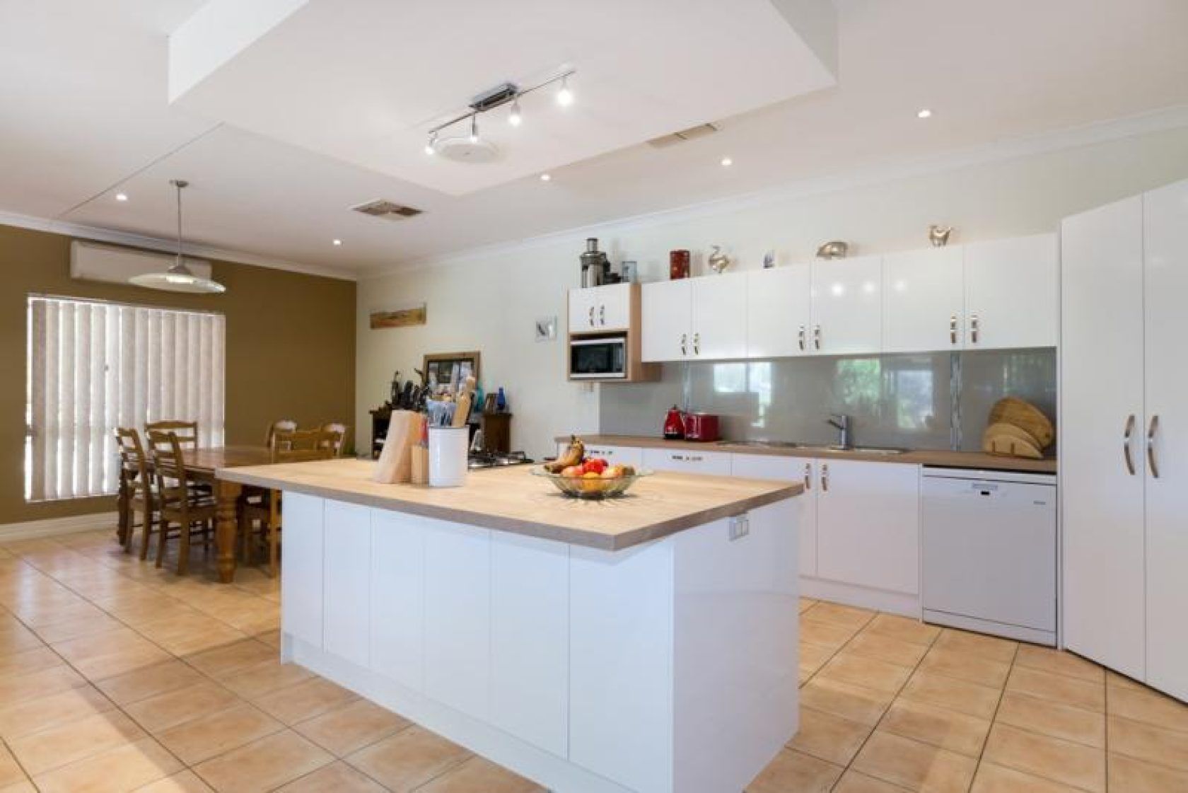 Spacious kitchen with a white island, cabinetry, and a dining table on a tiled floor.