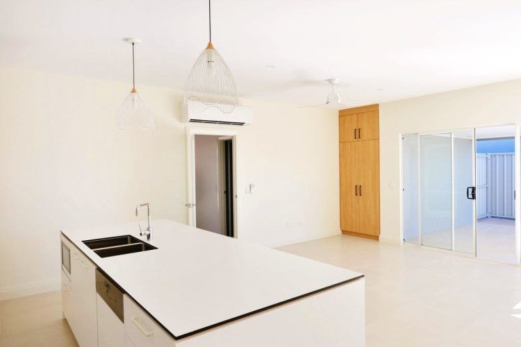 Bright, empty kitchen with white island, cabinets, and light fixtures. Doorway and folding door lead to other rooms.