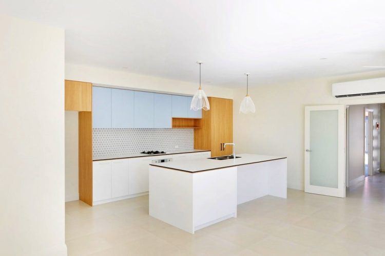 Modern kitchen with light blue and wood cabinets, white island, pendant lights, and open door.