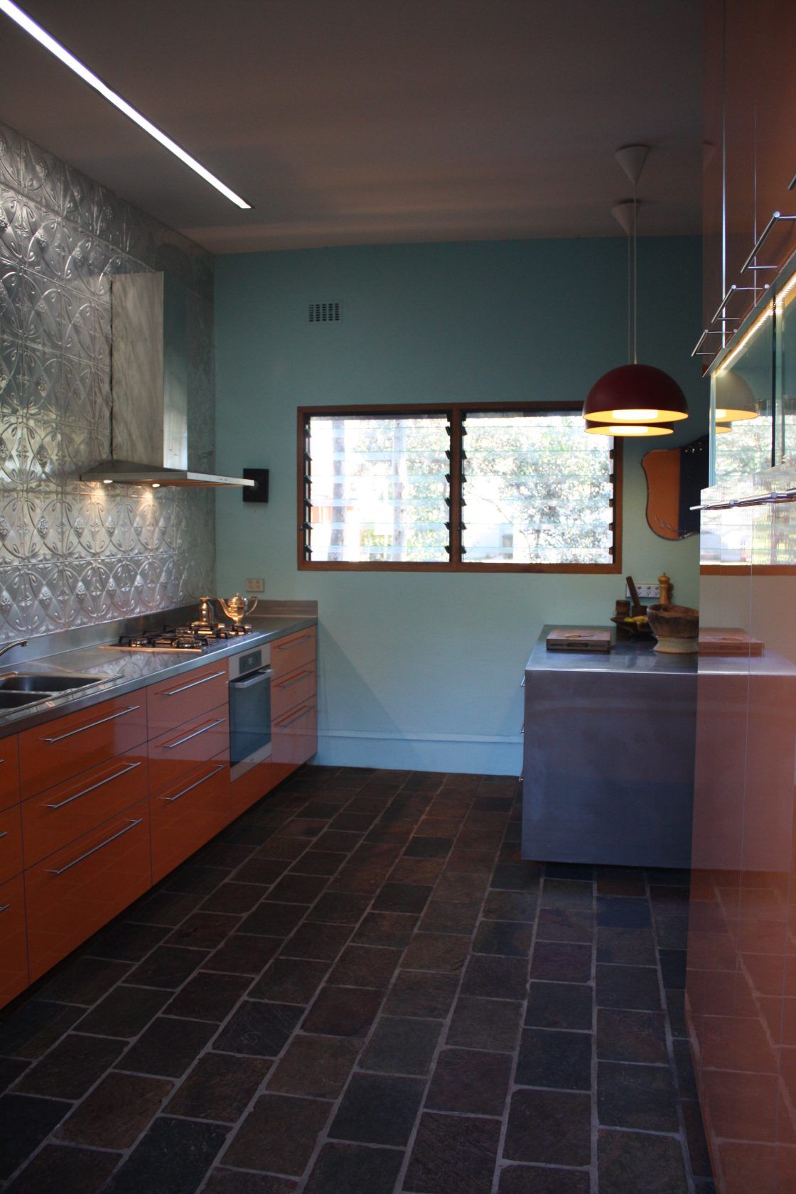 Orange kitchen with marble backsplash, blue walls, brown tile floor, and a window.
