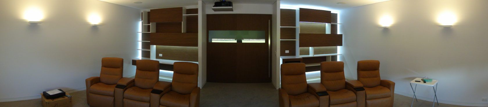 A home theater room with brown recliners facing a screen, lit by wall sconces.